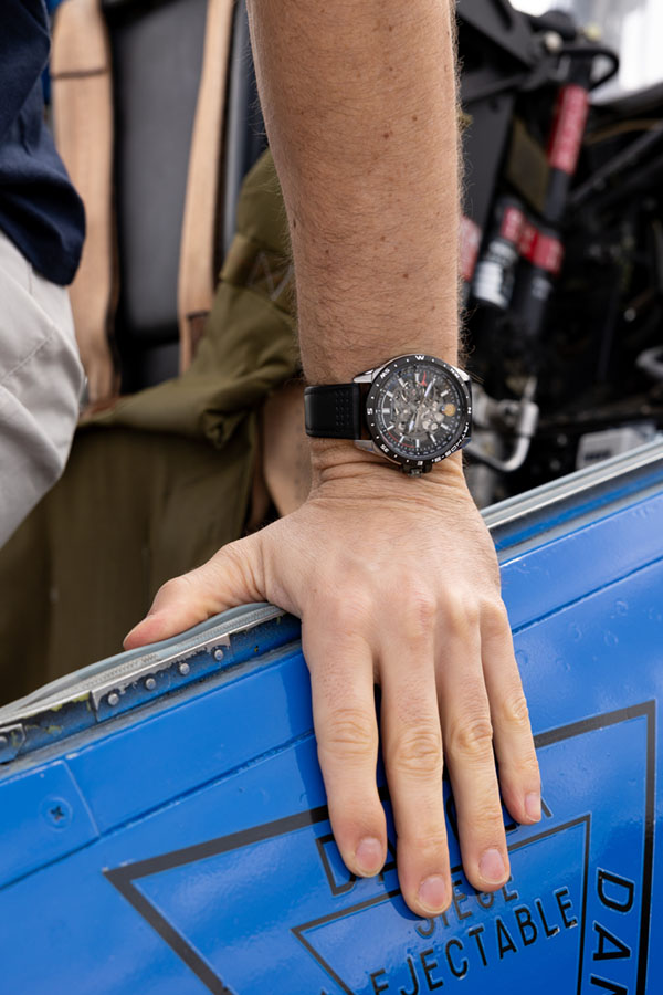 Montre patrouille de France avec bracelet en cuir noir, portée devant un avion alphajet de la Patrouille de France