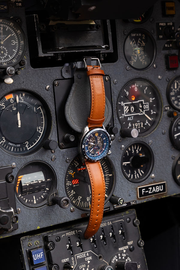 Montre patrouille de France avec bracelet en cuir marron et cadran bleu, posée sur le tableau de bord d'un alpha jet